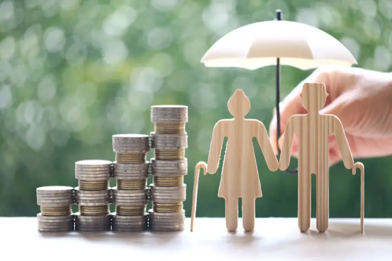 A wooden cut-out Figure of a older couple and a stack of coins next to them 